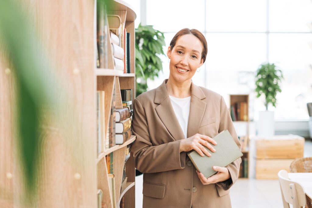 Adult smiling brunette business woman mentor reading book at green modern office